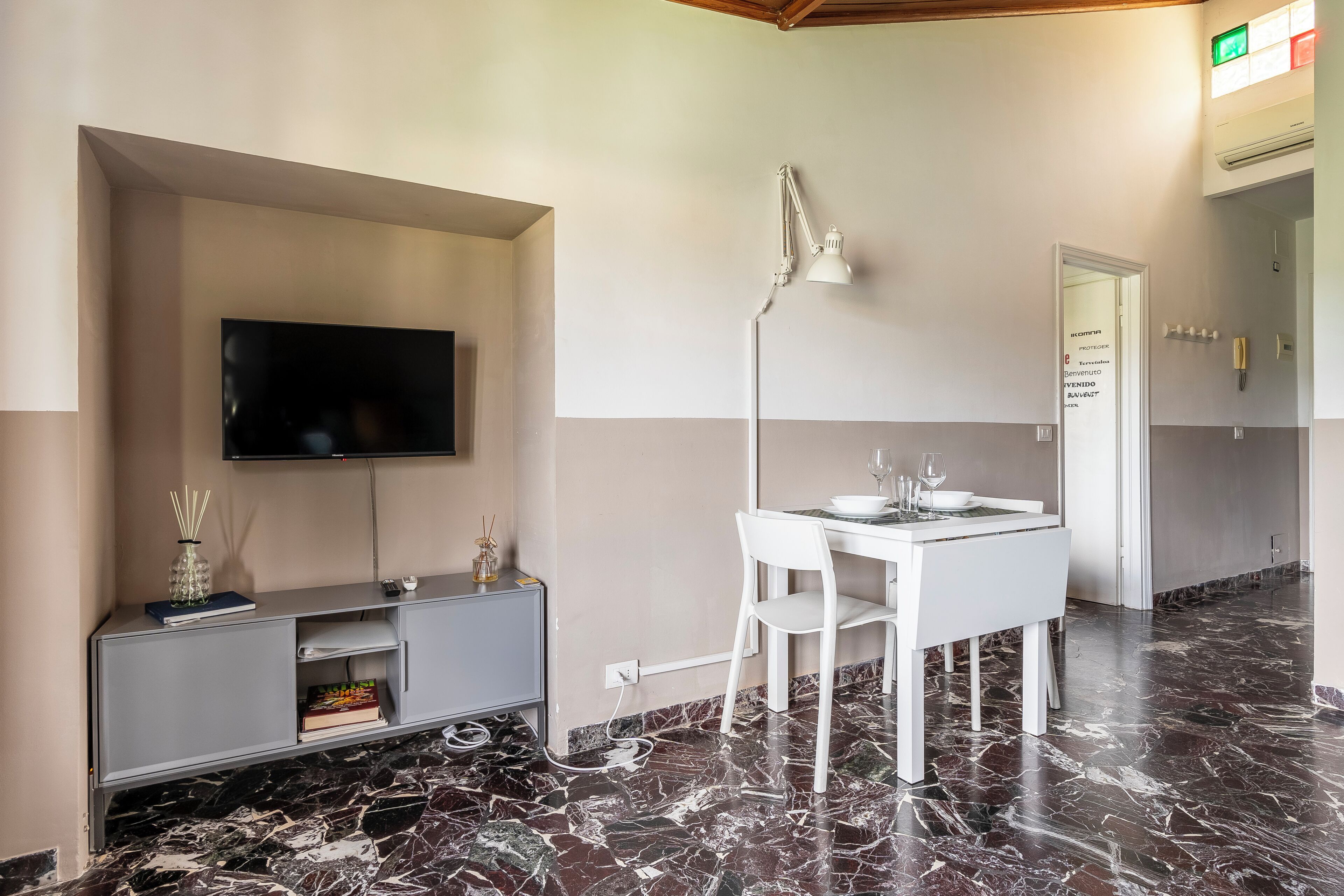 A modern room with a flat-screen TV, grey entertainment unit, white dining table, and chairs.