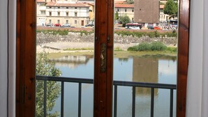 Une vue depuis une fenêtre à cadre en bois, donnant sur une rivière, une tour et des bâtiments surmontés d’un dôme.