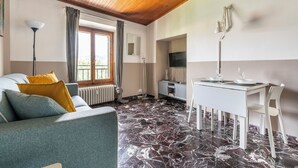 Une pièce avec un plafond en bois, un canapé avec des coussins, une table à manger avec des chaises, un téléviseur et un radiateur.