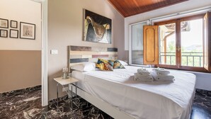 Une chambre d’hôtel avec un lit, des œuvres d’art, une fenêtre donnant sur un paysage agréable et un sol en marbre.