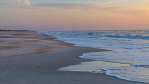 A beach with waves gently lapping onto the shore, a clear sky, and a distant pier. - Ocean View Beachfront Getaway Directly on St. Augustine Beach.  (St. Augustine Beach)