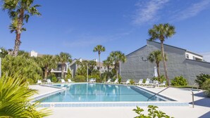 A swimming pool with lounge chairs, surrounded by palm trees and a building with a grey facade. - Ocean View Beachfront Getaway Directly on St. Augustine Beach.  (St. Augustine Beach)