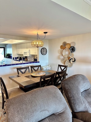 A dining area with a table set for four, a wall clock, and a decorative wall hanging. - Ocean View Beachfront Getaway Directly on St. Augustine Beach. (St. Augustine Beach)