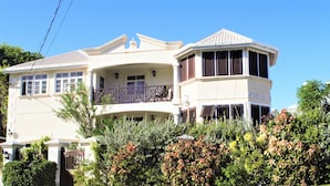 A two-story house with a balcony, a gated entrance, and a variety of plants in the front yard.
