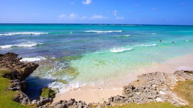 A beach with clear turquoise water, rocky shoreline, and a few people swimming.