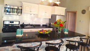 A kitchen with white cabinets, stainless steel appliances, a black countertop, and a central island with chairs.