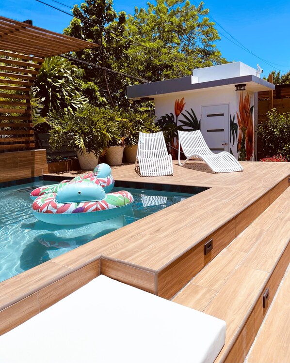 A pool area with lounge chairs, a floating pool float, and potted plants.