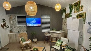 Una sala de estar moderna con televisor, sillas de mimbre, una mesa de centro y plantas decorativas.