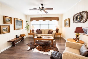 A living room with a sofa, coffee table, and a cowhide rug. There are framed pictures on the walls, a ceiling fan, and a window with blinds. - Boutique Farm Stay — Thoughtfully Designed (Georgetown)