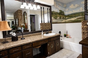 A bathroom with a large mirror, a sink, a vanity with drawers, a bathtub, and a stone wall. - Boutique Farm Stay — Thoughtfully Designed (Georgetown)