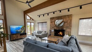 A spacious living room with a large grey sofa, a flat-screen TV, a fireplace, and a stone accent wall.