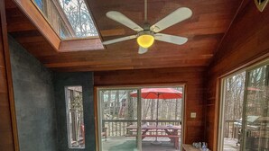 A spa area with a hot tub, wooden flooring, a ceiling fan, and large windows offering views of the outdoors.