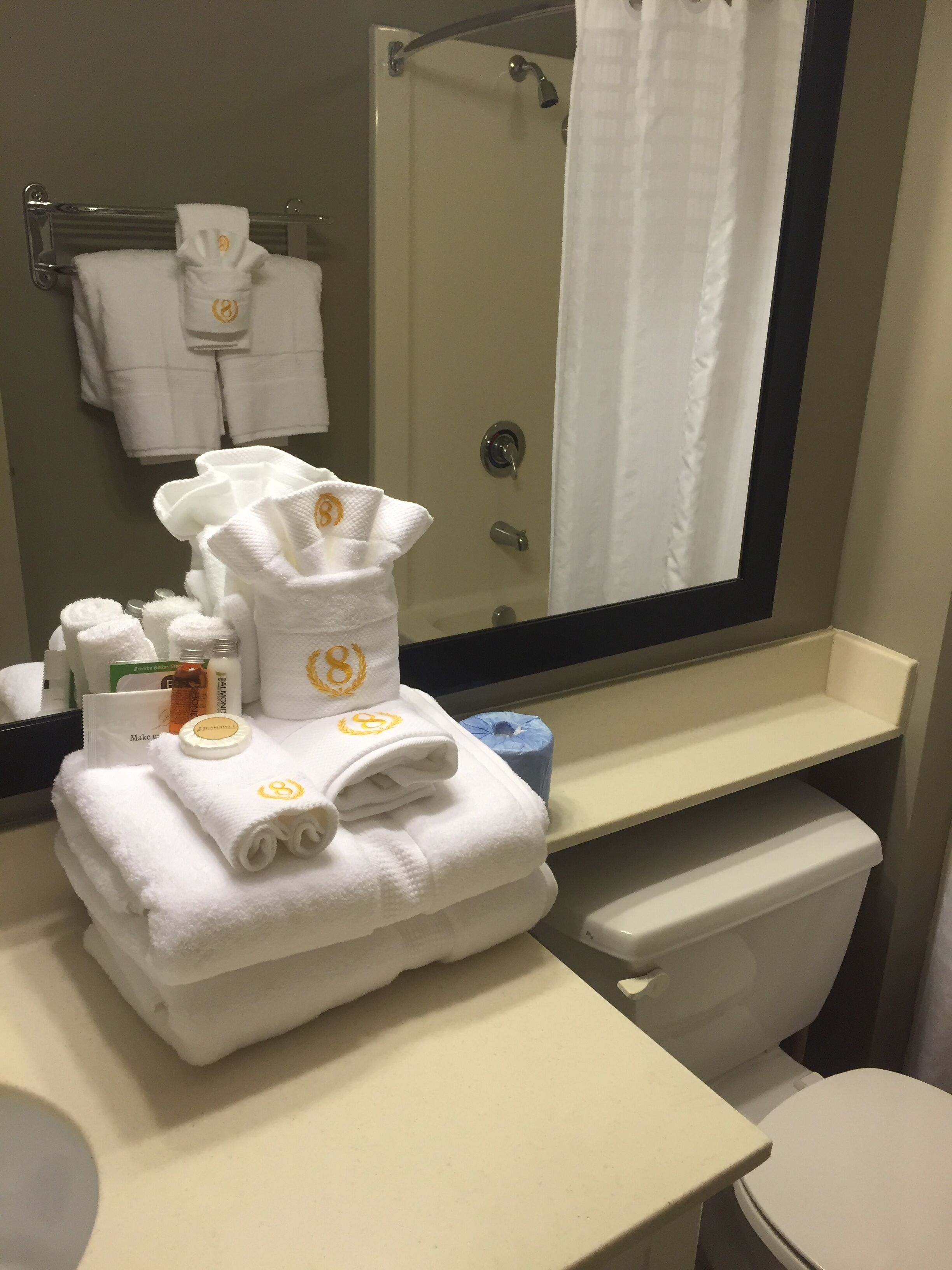 A bathroom with a sink, mirror, and toilet. There are towels stacked on the sink, and toiletries are visible on the counter.