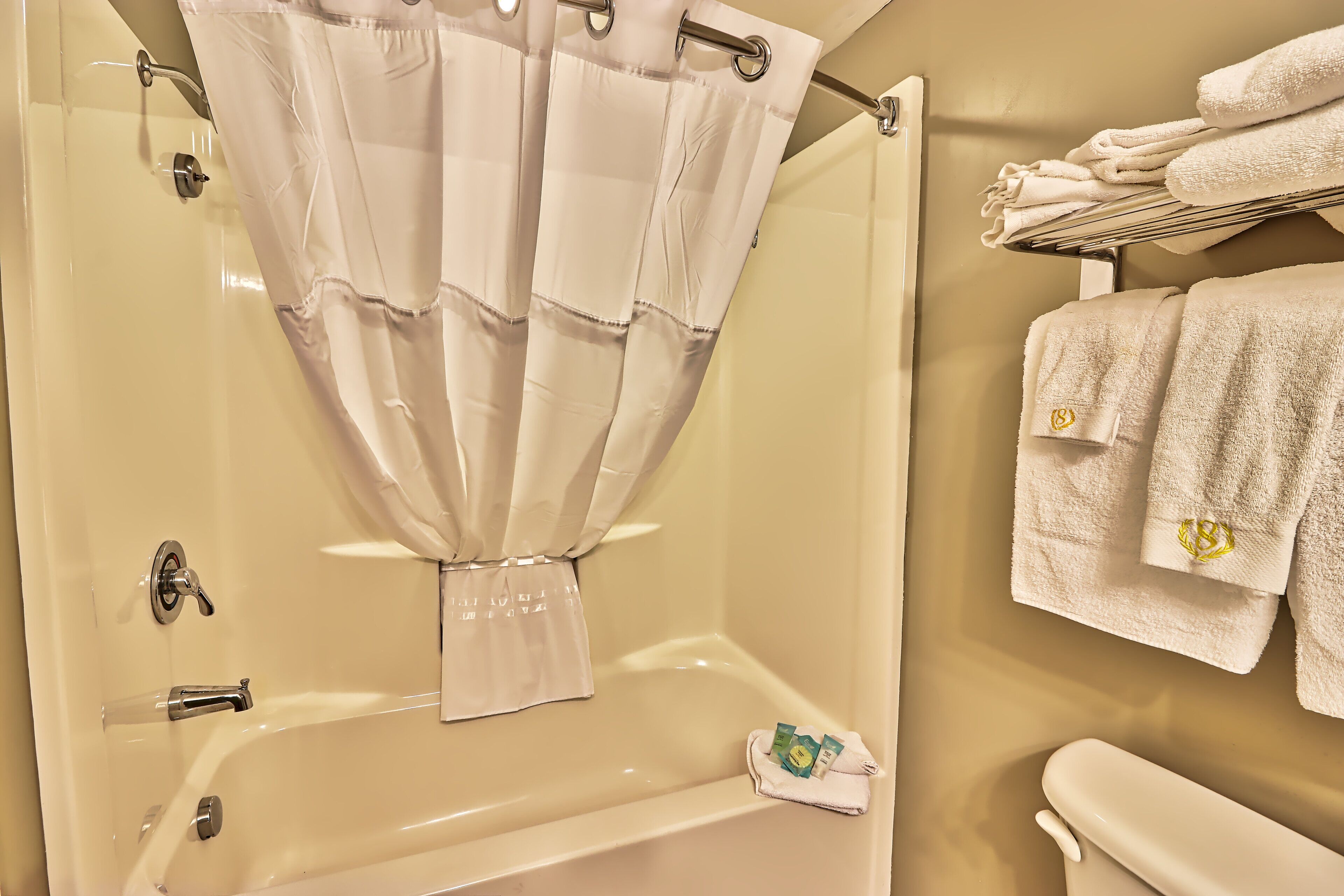 A bathroom with a bathtub, a shower curtain, a towel rack with towels, and a toilet.
