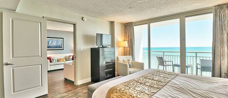 A hotel room with a large bed, a TV, a desk, and a view of the sea.