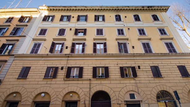 Een meerlaags gebouw met een uniforme architectuur, met boogvormige deuropeningen en ramen voorzien van luiken.