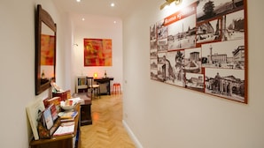 Een gang met een aan de muur bevestigde fotocollage met de titel 'Roma sparta', een houten bureau met boeken, een stoel en een kleine tafel met een fles.