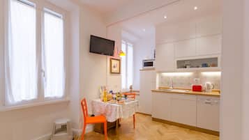 Una cucina moderna con mobili bianchi, un tavolo da pranzo con sedie arancioni e una TV a parete.
