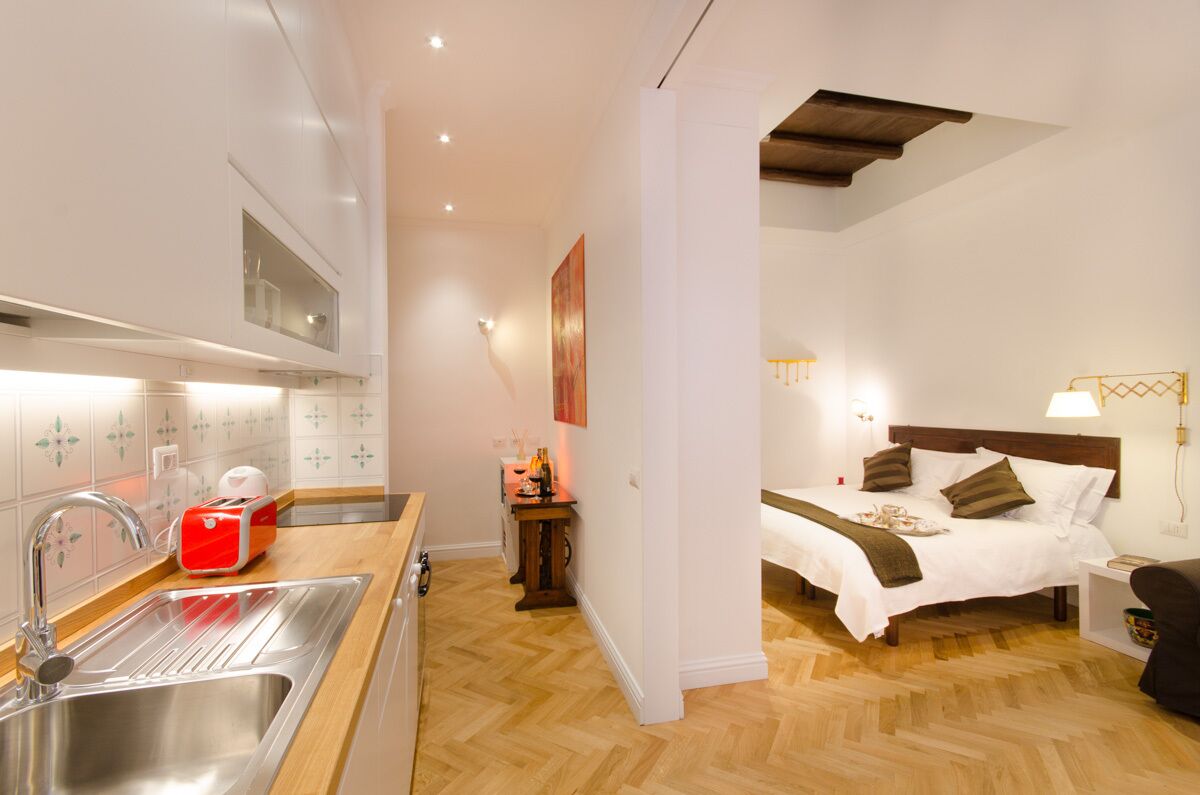Ein kompaktes Hotelzimmer mit Küchenzeile, einem Bett mit Holz-Kopfteil und einem kleinen Nachttisch.
