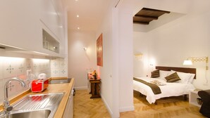 Een compacte hotelkamer met kitchenette, een bed met houten hoofdeinde en een klein nachtkastje.