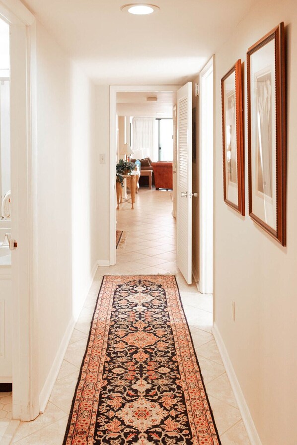 A hallway with a patterned rug, white walls, and framed pictures on the right.