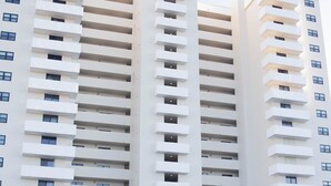 Un hôtel à plusieurs étages au design moderne, doté de balcons à chaque niveau et d’un parking pouvant accueillir plusieurs voitures.