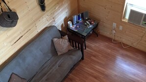 Ein gemütliches Holzhütten-Interieur mit einer Couch, einem kleinen Tisch mit Fernseher und einem Fenster mit Klimaanlage.