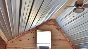 Ein kleines, gemütliches Schlafzimmer im Dachgeschoss mit schrägen Wänden, einem Einzelbett, einem kleinen Tisch und einem Fenster mit Lüftung.