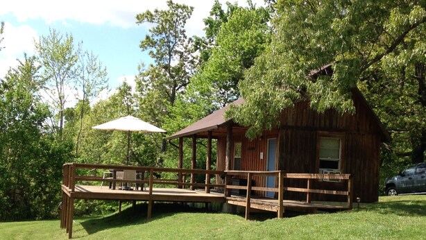 Eine rustikale Holzhütte mit einer Veranda, umgeben von üppigem Grün.