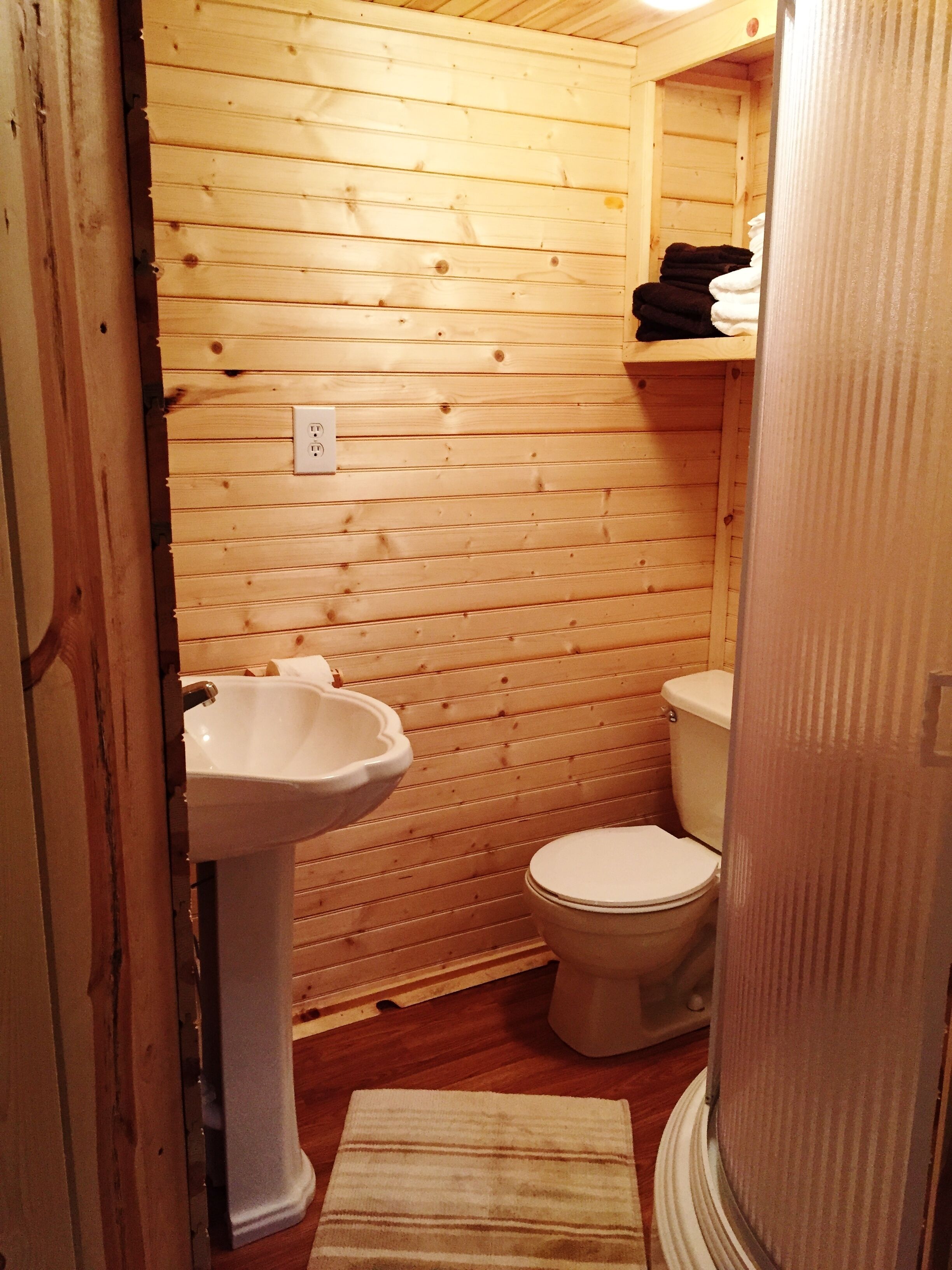 Un baño pequeño con paneles de madera, un lavabo blanco y un inodoro, con una toalla en el suelo.