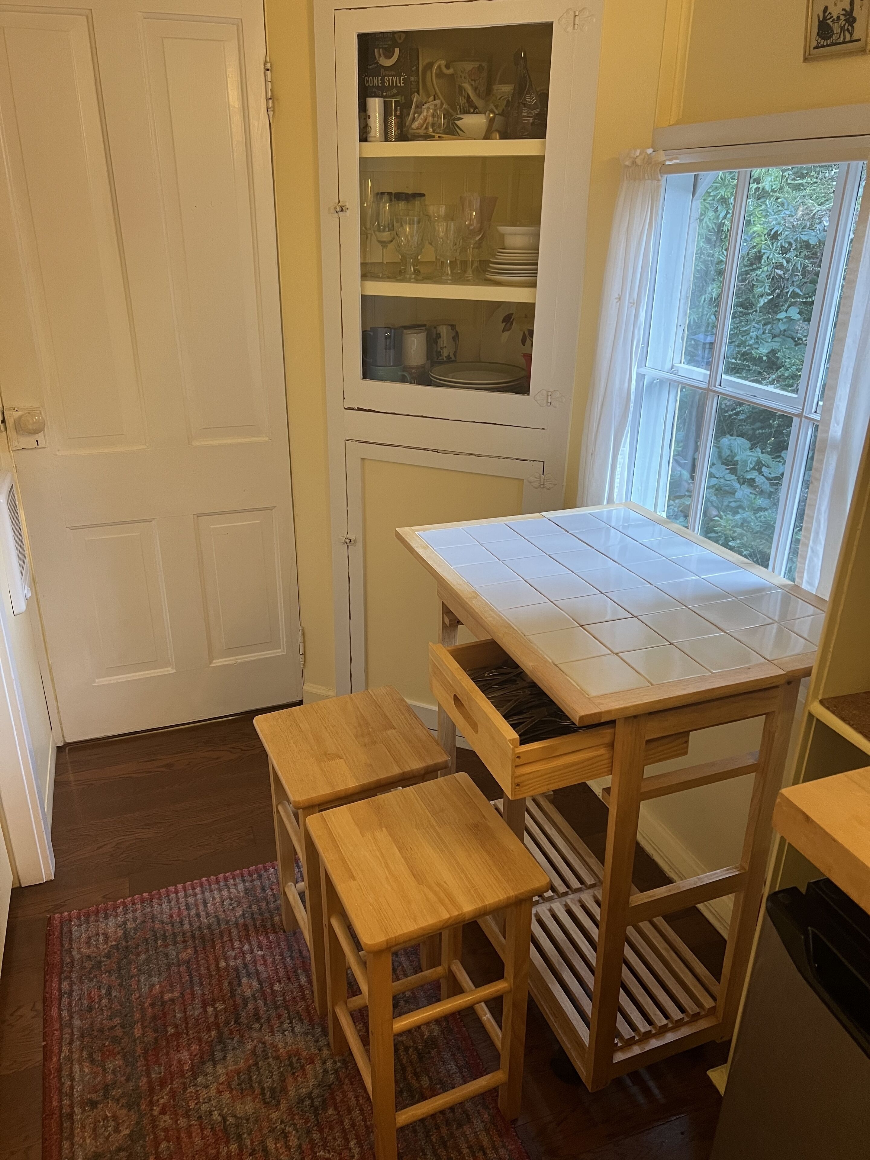 Una cocina con un armario blanco, una ventana y una mesa con azulejos.