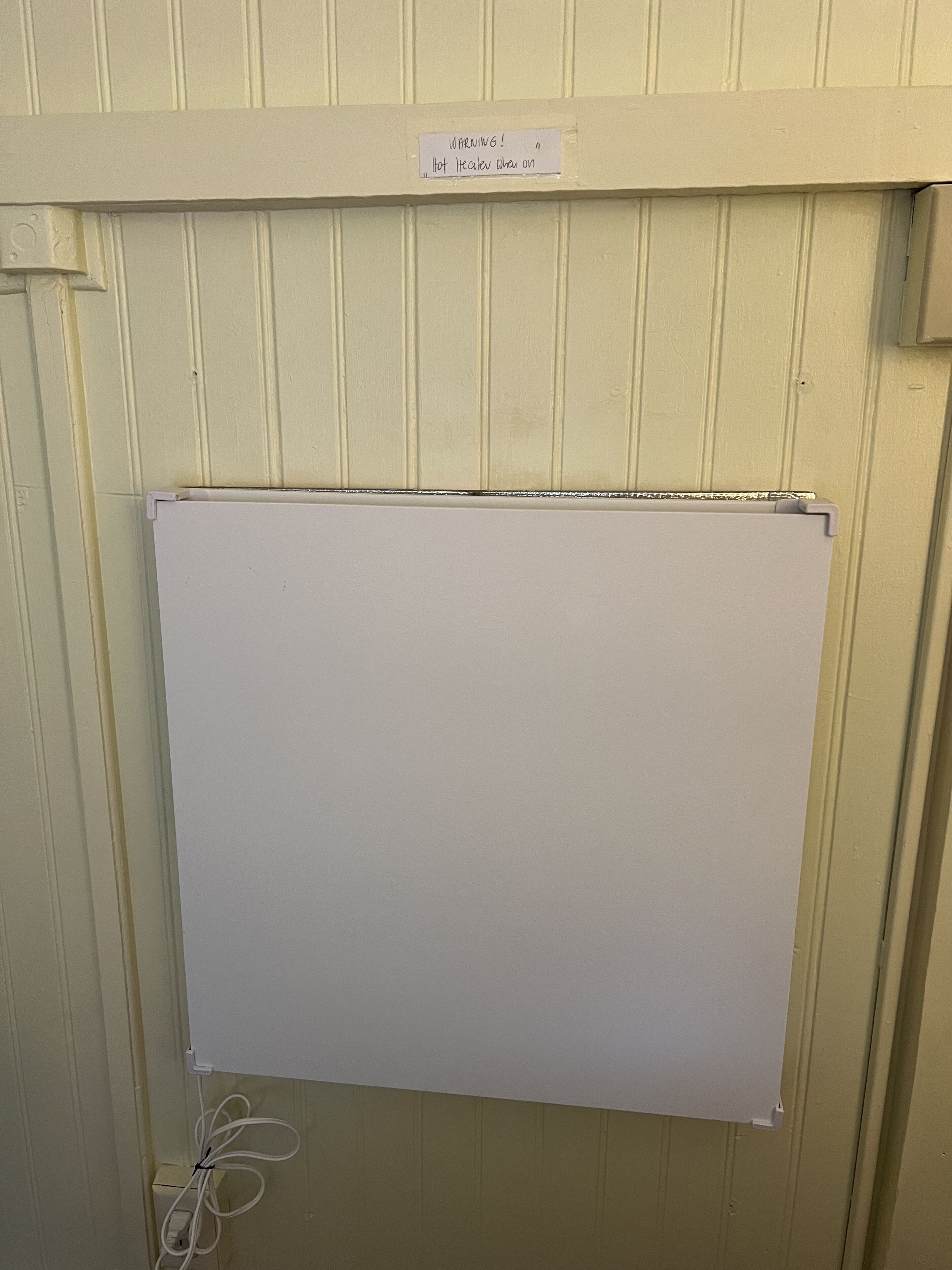 A whiteboard mounted on a wall with a warning sign above it.