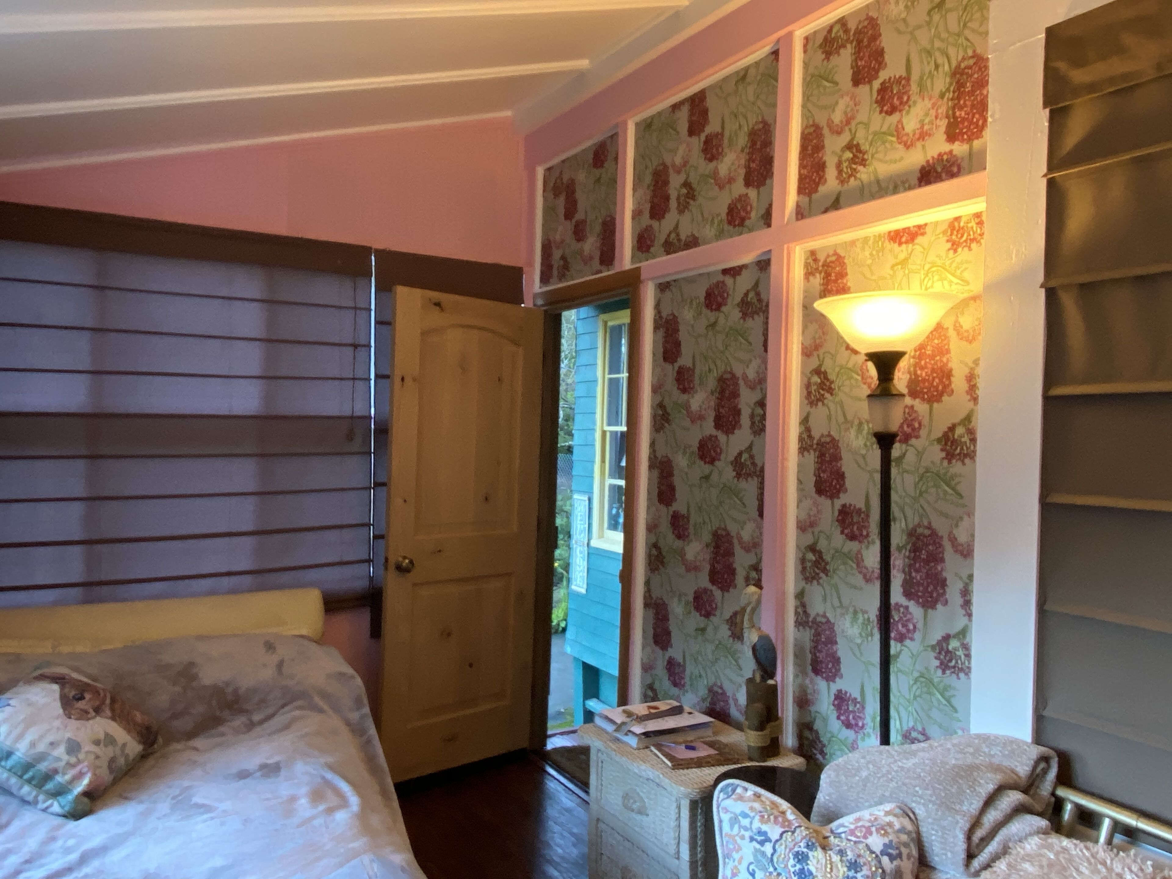 Une chambre à coucher comprenant un lit, une commode, une chaise et une fenêtre ornée d’un papier peint à motifs floraux.