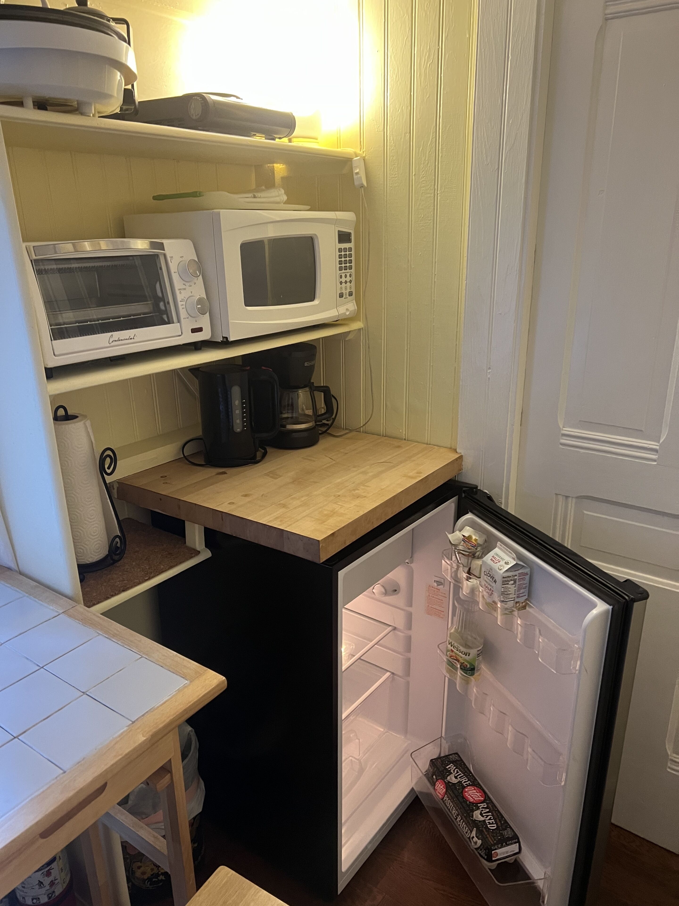 A compact kitchenette with a microwave, toaster, and coffee maker on a wooden countertop.