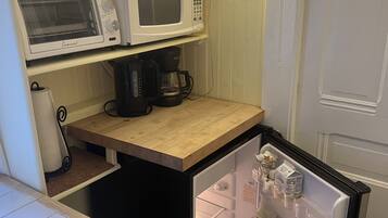 A compact kitchenette with a microwave, toaster, and coffee maker on a wooden countertop.