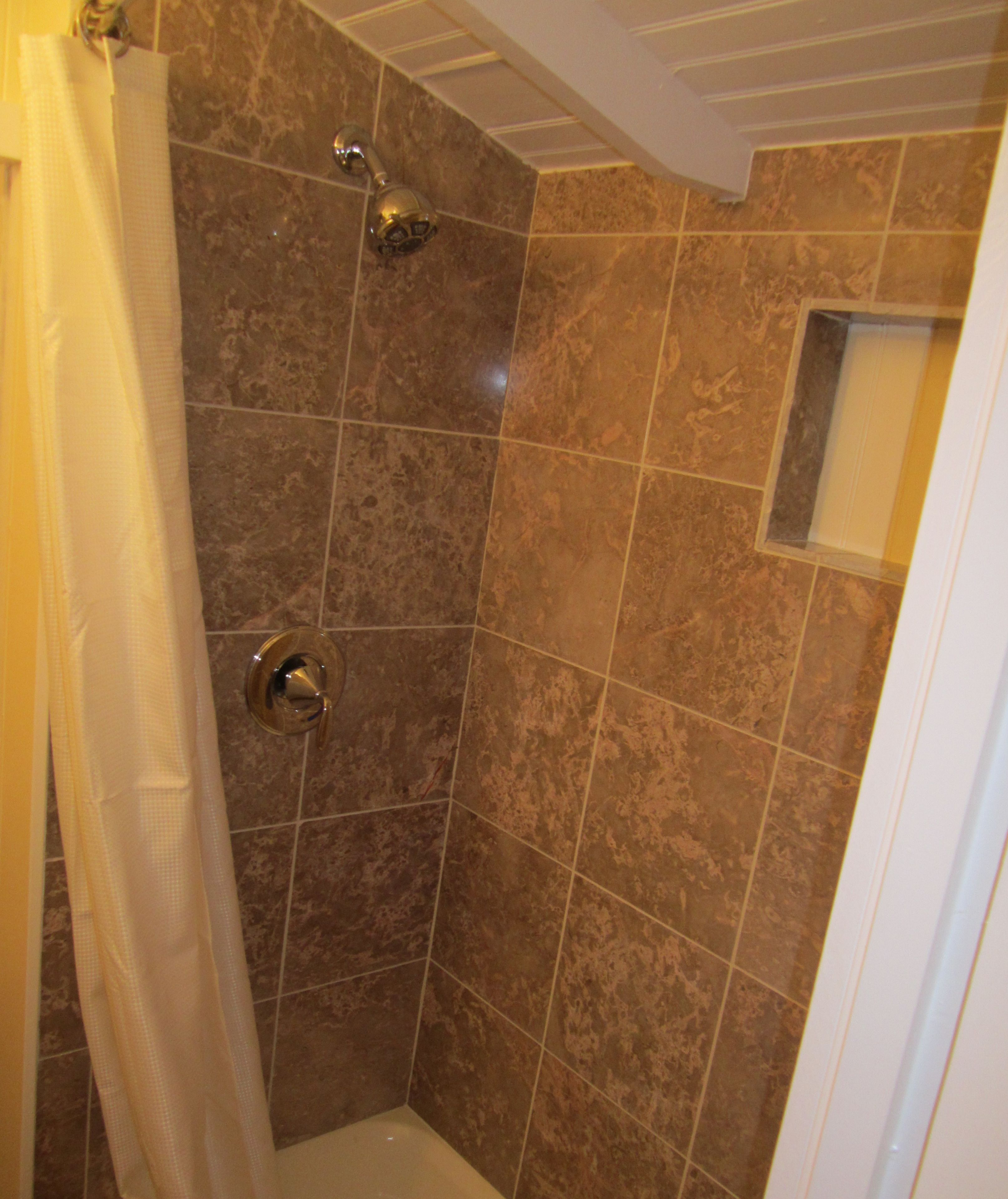 A shower with a glass door, a showerhead, and a small window.