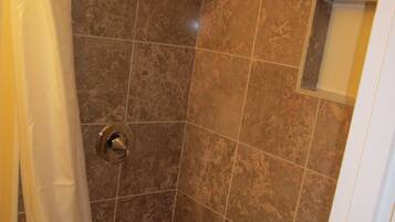 A shower with a glass door, a showerhead, and a small window.