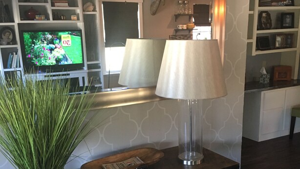 Una sala de estar con televisor, lámpara, planta y cesta de frutas sobre una consola.