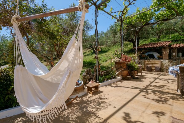 Un hamac suspendu à un arbre, un bâtiment en pierre d’aspect rustique et un espace patio aménagé avec du mobilier d’extérieur.