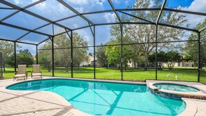 Una piscina con cerramiento de vidrio, rodeada por un patio de ladrillo y dos sillas de descanso.