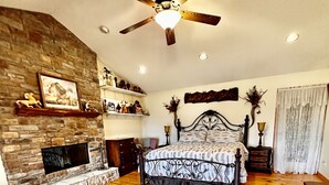 A spacious bedroom with a large bed, a fireplace, wooden flooring, and a ceiling fan. - Big Cabin on HorseRanch close to MammothCaves,Corvettes,WKU, BeechBend Buc-ees (Smiths Grove)