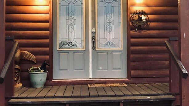 A wooden cabin with a double door featuring decorative glass panels, a porch with a potted plant, and a light fixture above the door. - Big Cabin on HorseRanch close to MammothCaves,Corvettes,WKU, BeechBend Buc-ees (Smiths Grove)