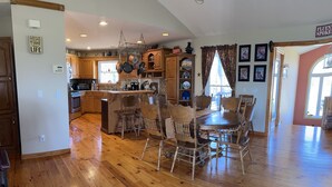 A spacious kitchen with wooden flooring, a central island, and a dining area with a wooden table and chairs. - Big Cabin on HorseRanch close to MammothCaves,Corvettes,WKU, BeechBend Buc-ees (Smiths Grove)