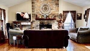 A spacious living room with a stone fireplace, a ceiling fan, and a television. - Big Cabin on HorseRanch close to MammothCaves,Corvettes,WKU, BeechBend Buc-ees (Smiths Grove)