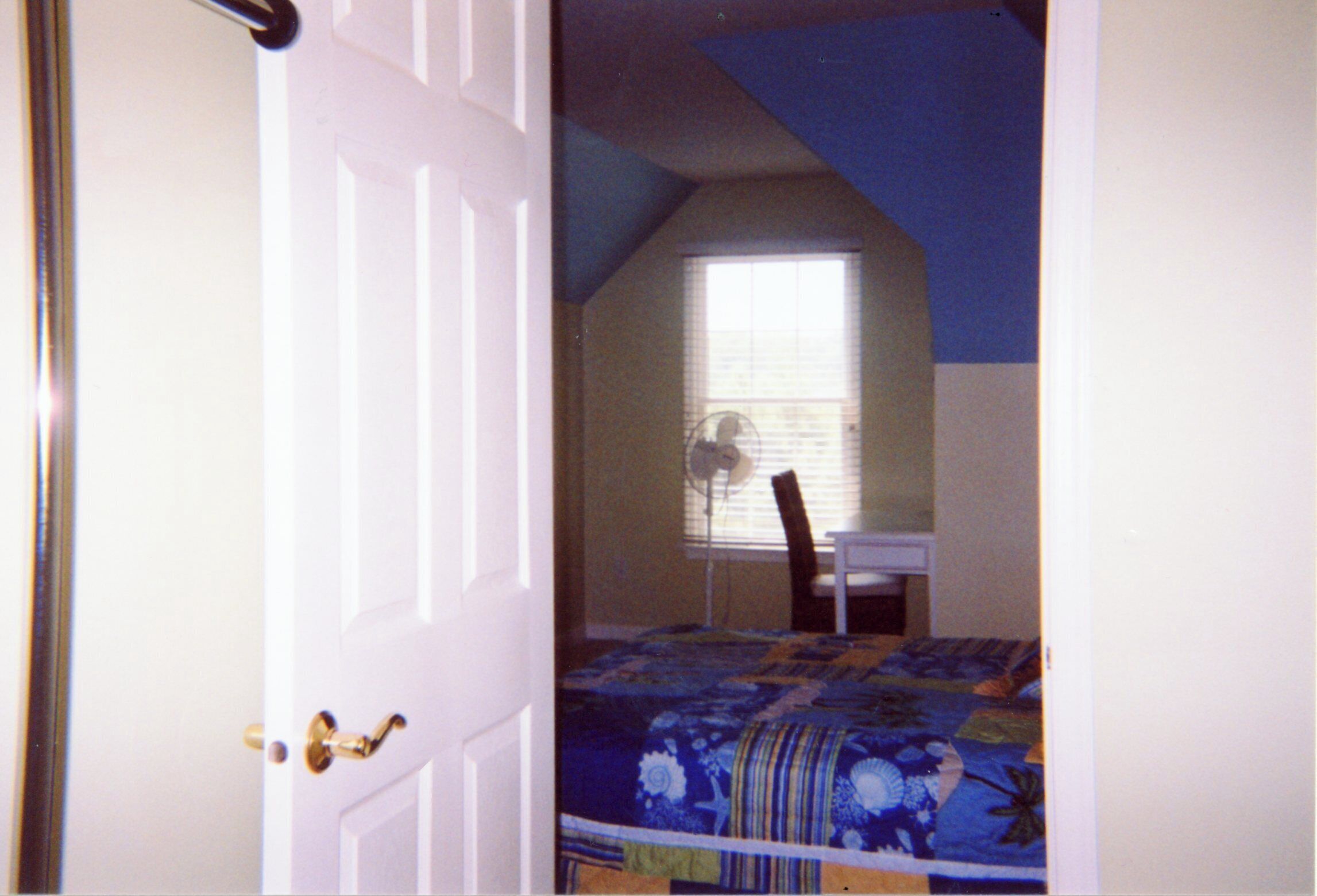 Quarto com cama, cadeira, escrivaninha e janela com cortinas.