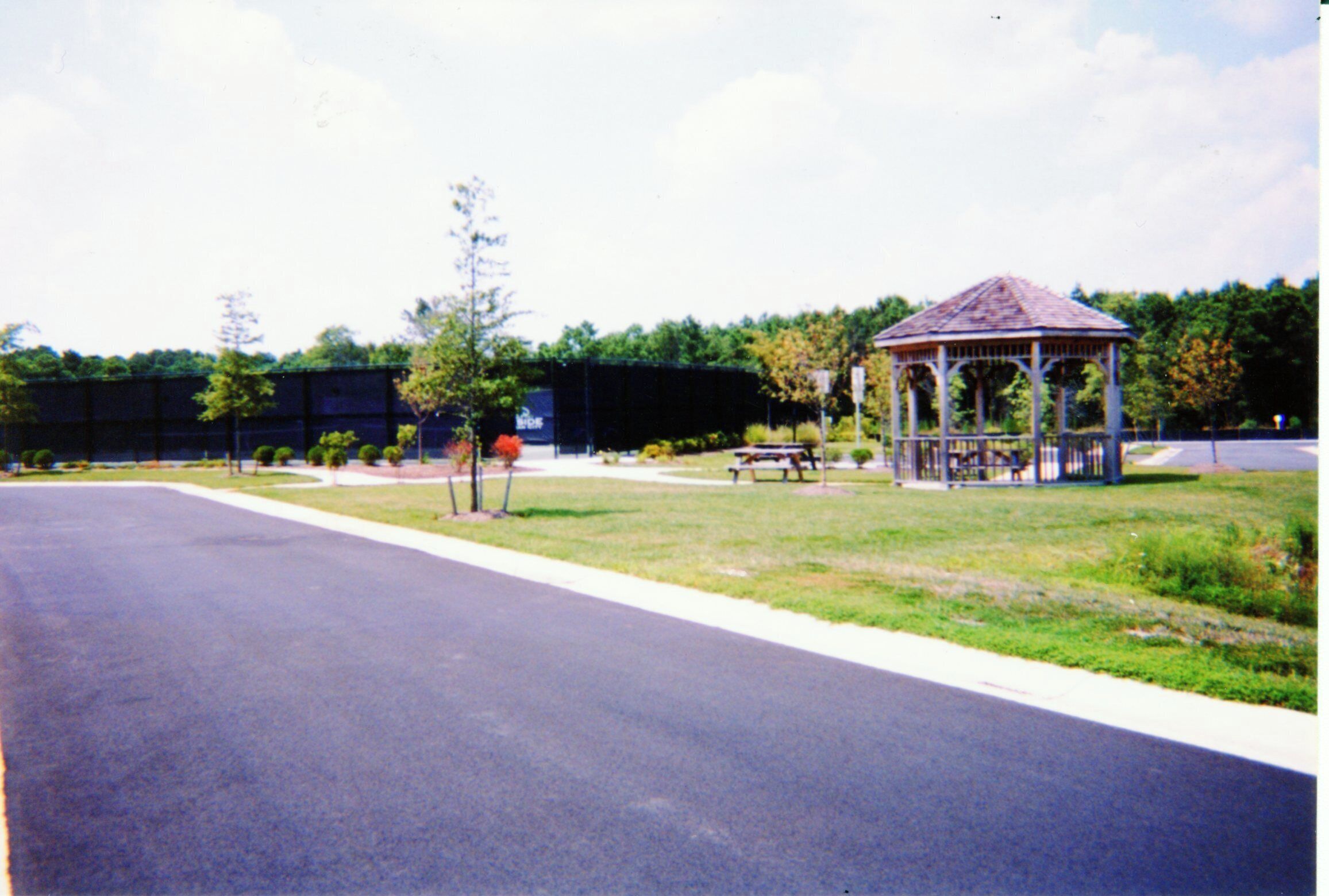 Un kiosque dans un parc, avec un chemin pavé et une clôture en arrière-plan.