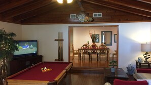A living room with a pool table, a television, a dining area with a table and chairs, and a ceiling fan.