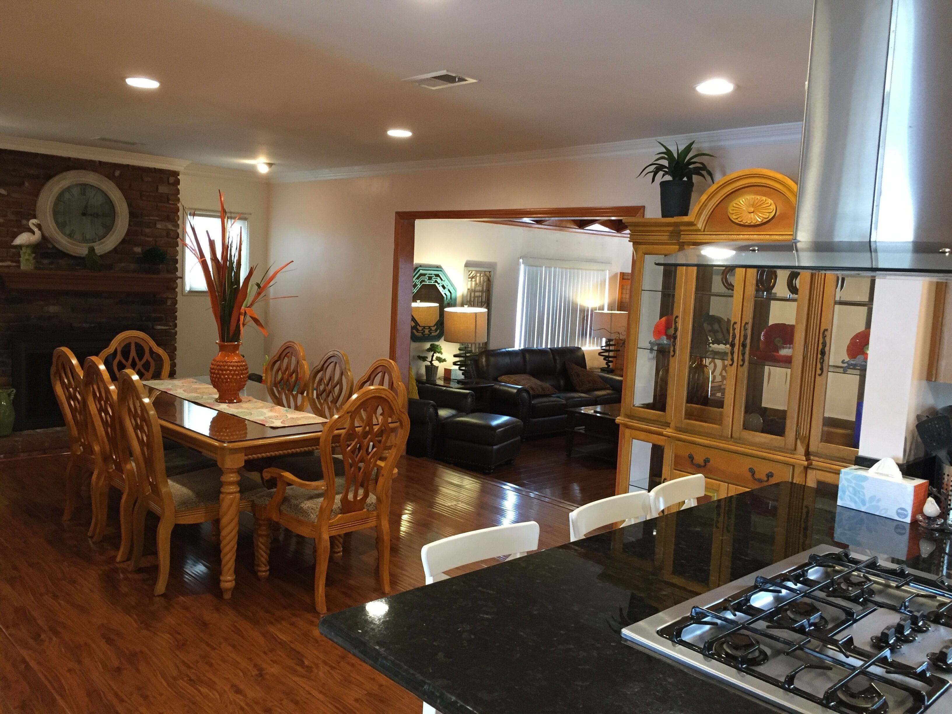 A dining area with wooden chairs and a table, a living room with a sofa and a lamp, and a kitchen with a stove.