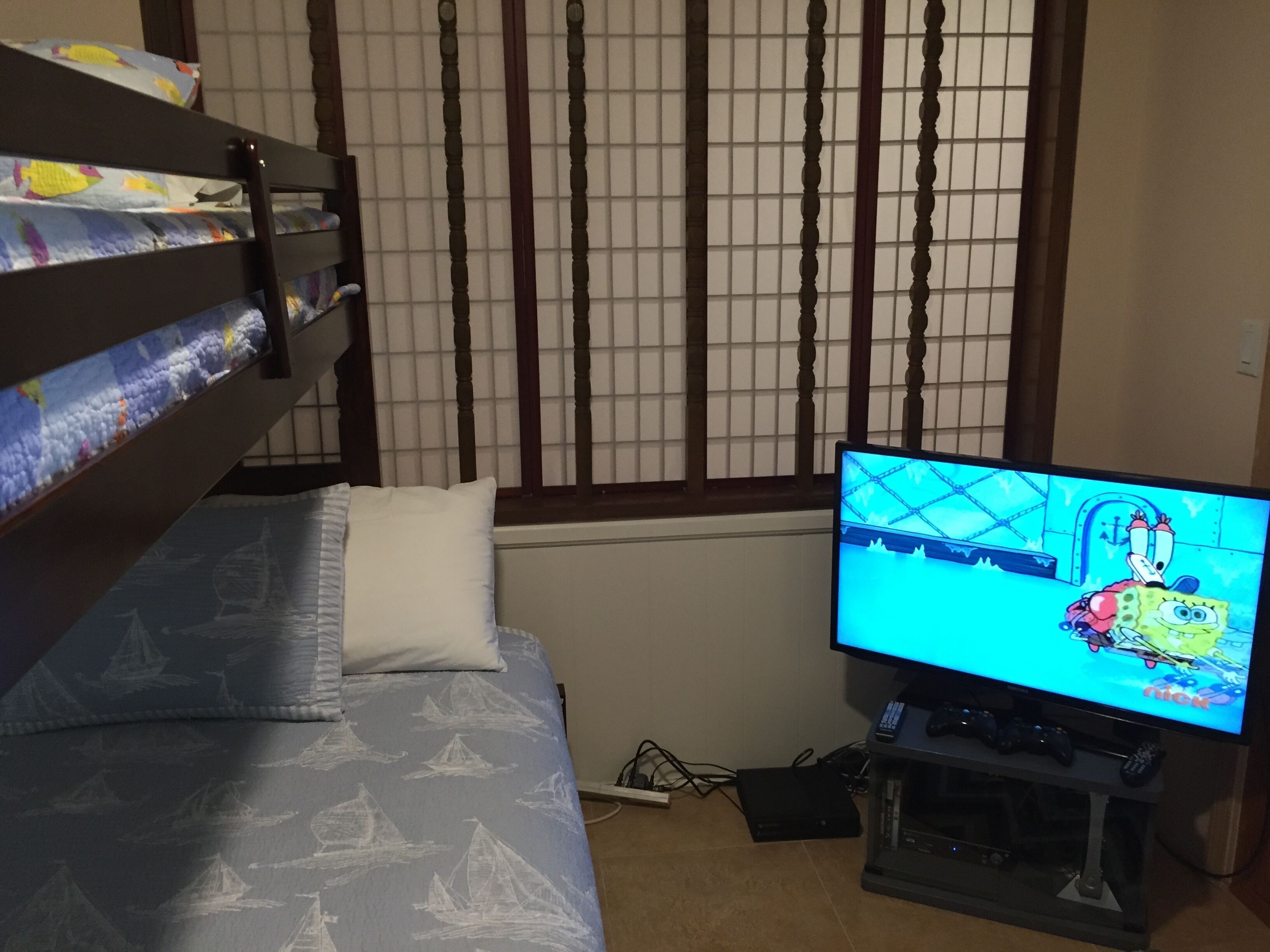 Een slaapkamer met een stapelbed, een televisie waarop een tekenfilm draait en een raam met zonwering.