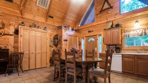 A wooden cabin interior with a dining table, chairs, a kitchen area, and a large window. - Two Master Suites, Great for 2 couples, Walking distance to Thunder Ridge Arena (Ridgedale)